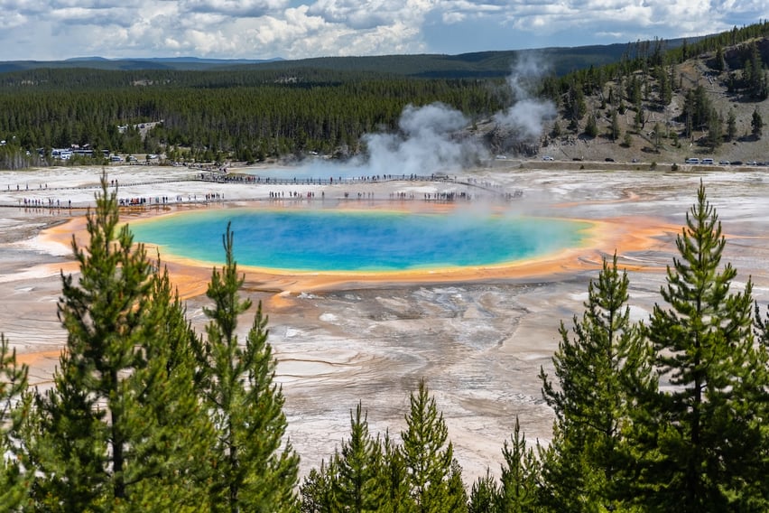 People walking around boardwalks at the Grand Prismatic Spring as viewed from the overlook trail in Yellowstone National Park.