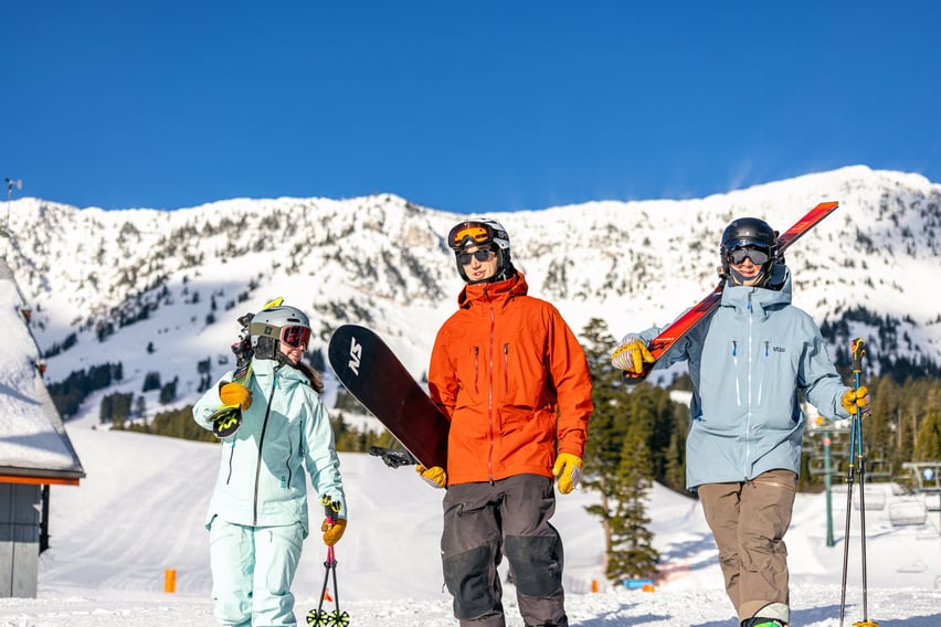Two skiiers and a snowboarder walking at Bridger Bowl.