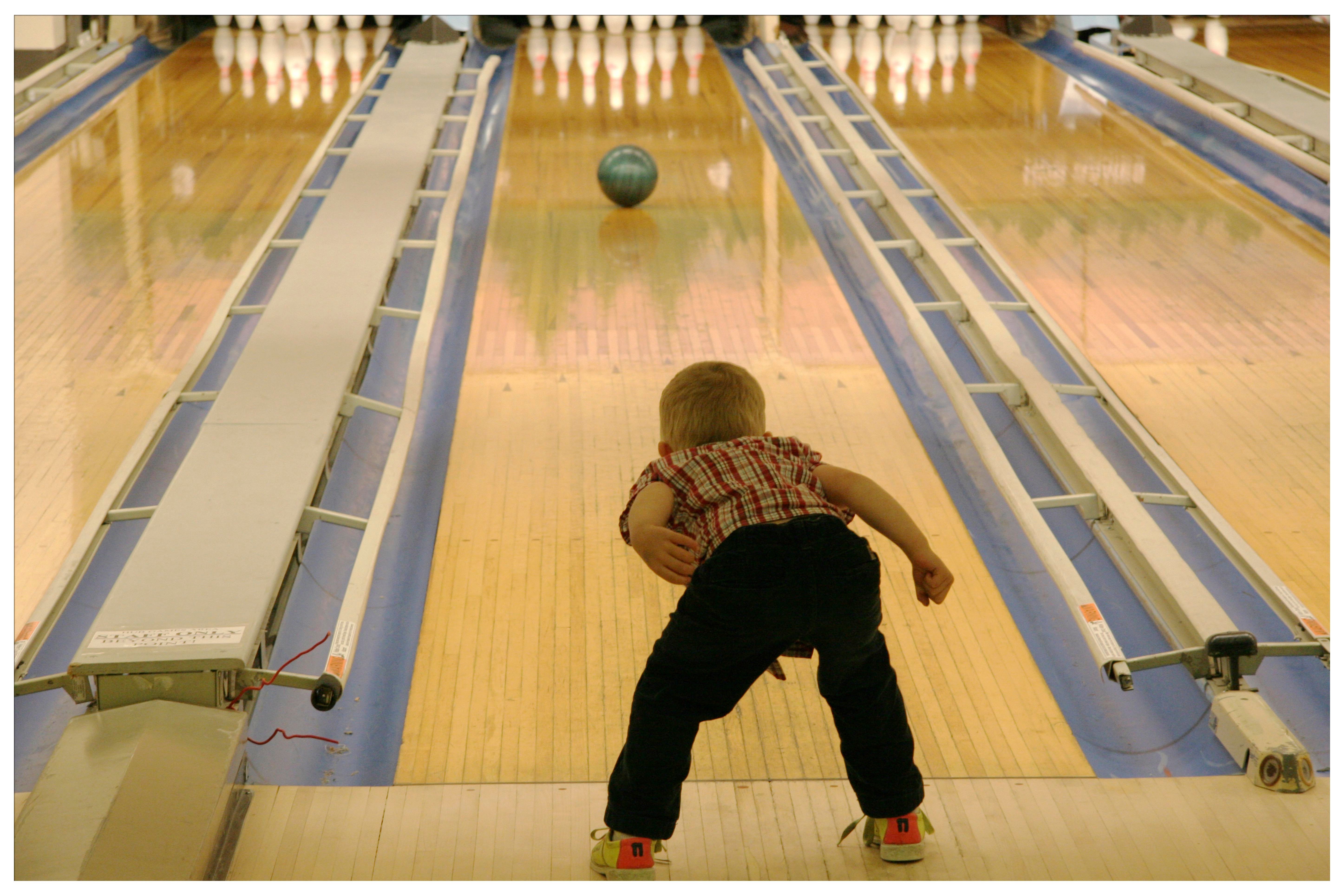 Little kid bowling at a bowling alley.