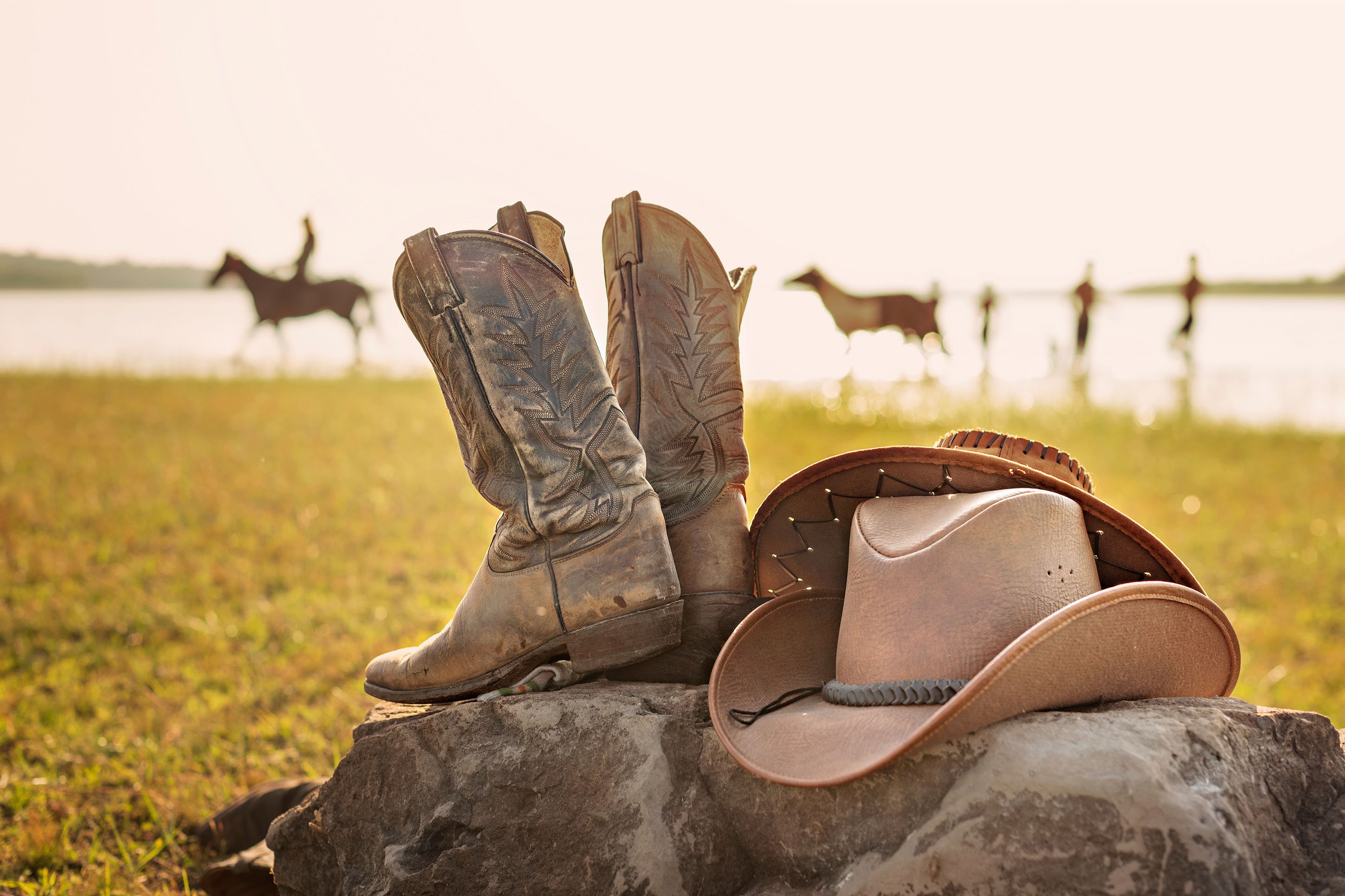 photo of western boots & hats sitting on rocks with a ranch background