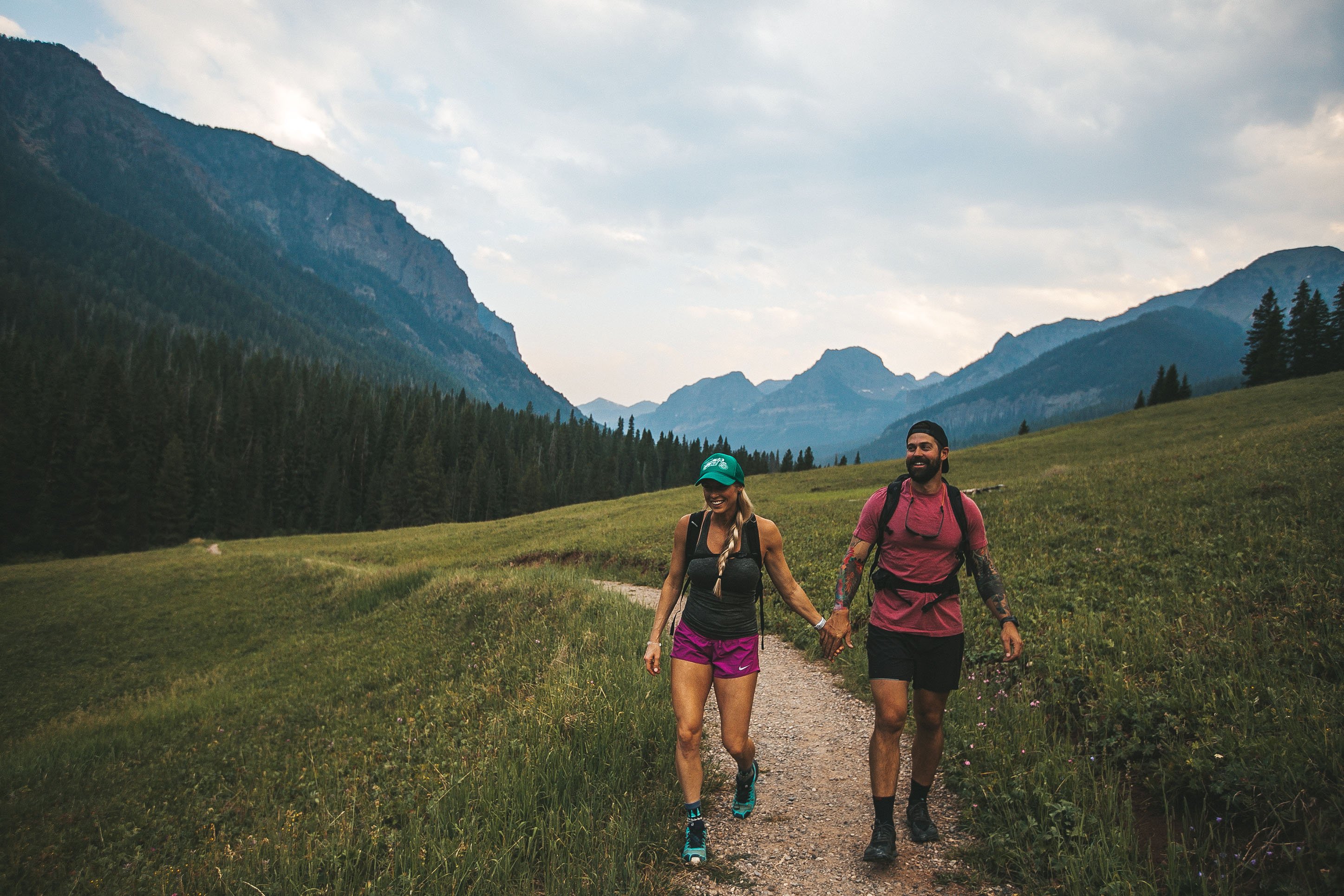 Photo of a couple holding hands while hiking in a green valley with mountains in the background