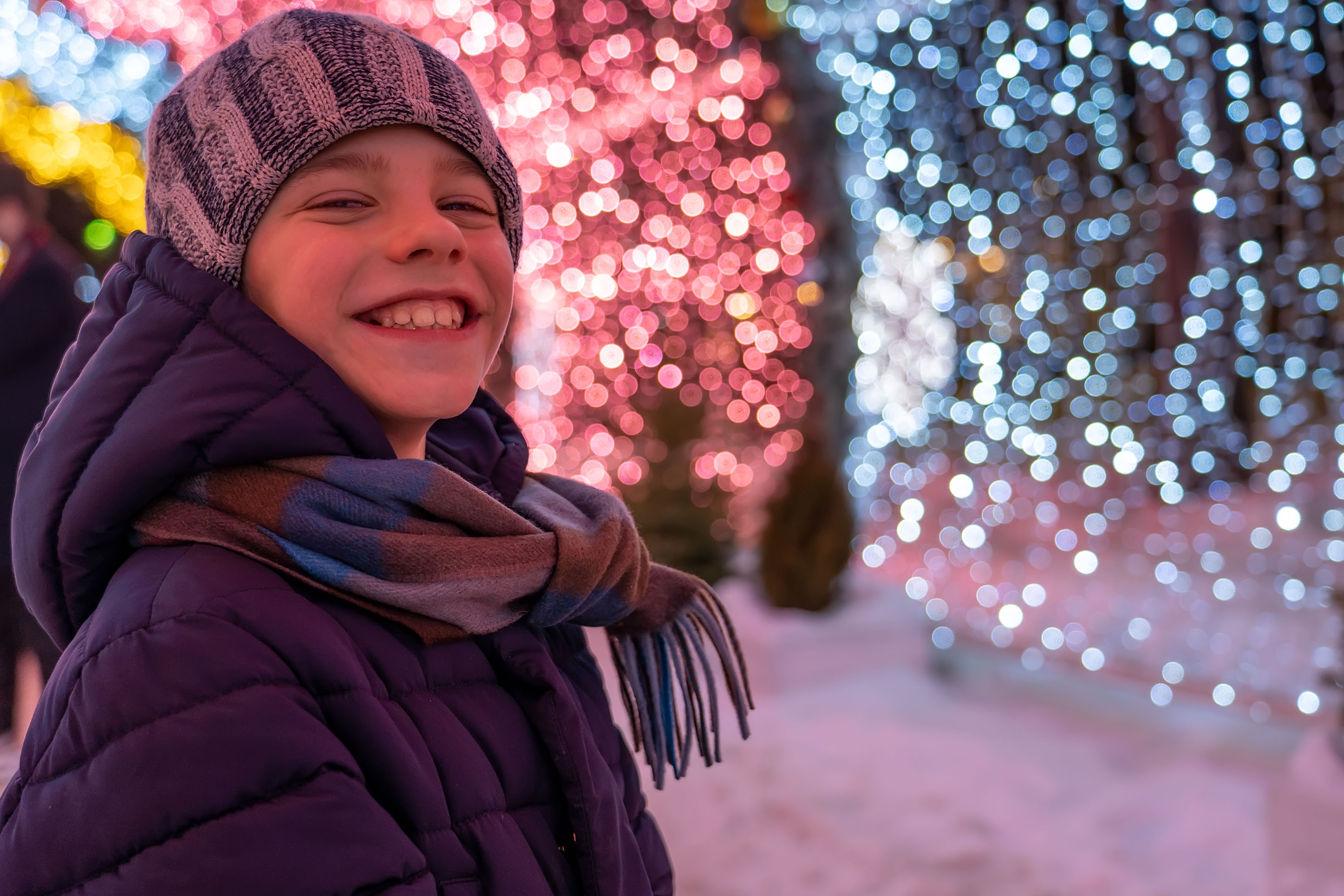 photo of a child smiling in winter clothing in front of a holiday light display
