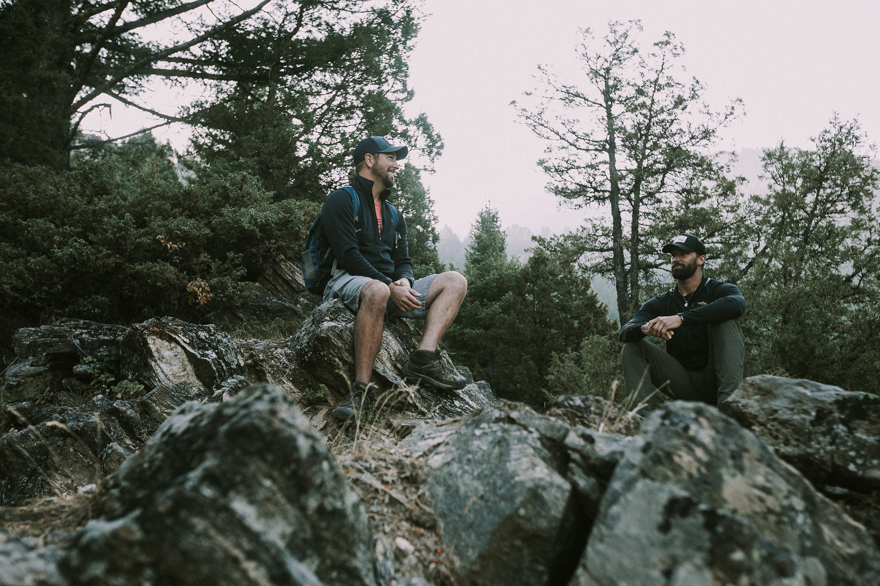 Photo of two men having a conversation sitting on rocks, smiling. 