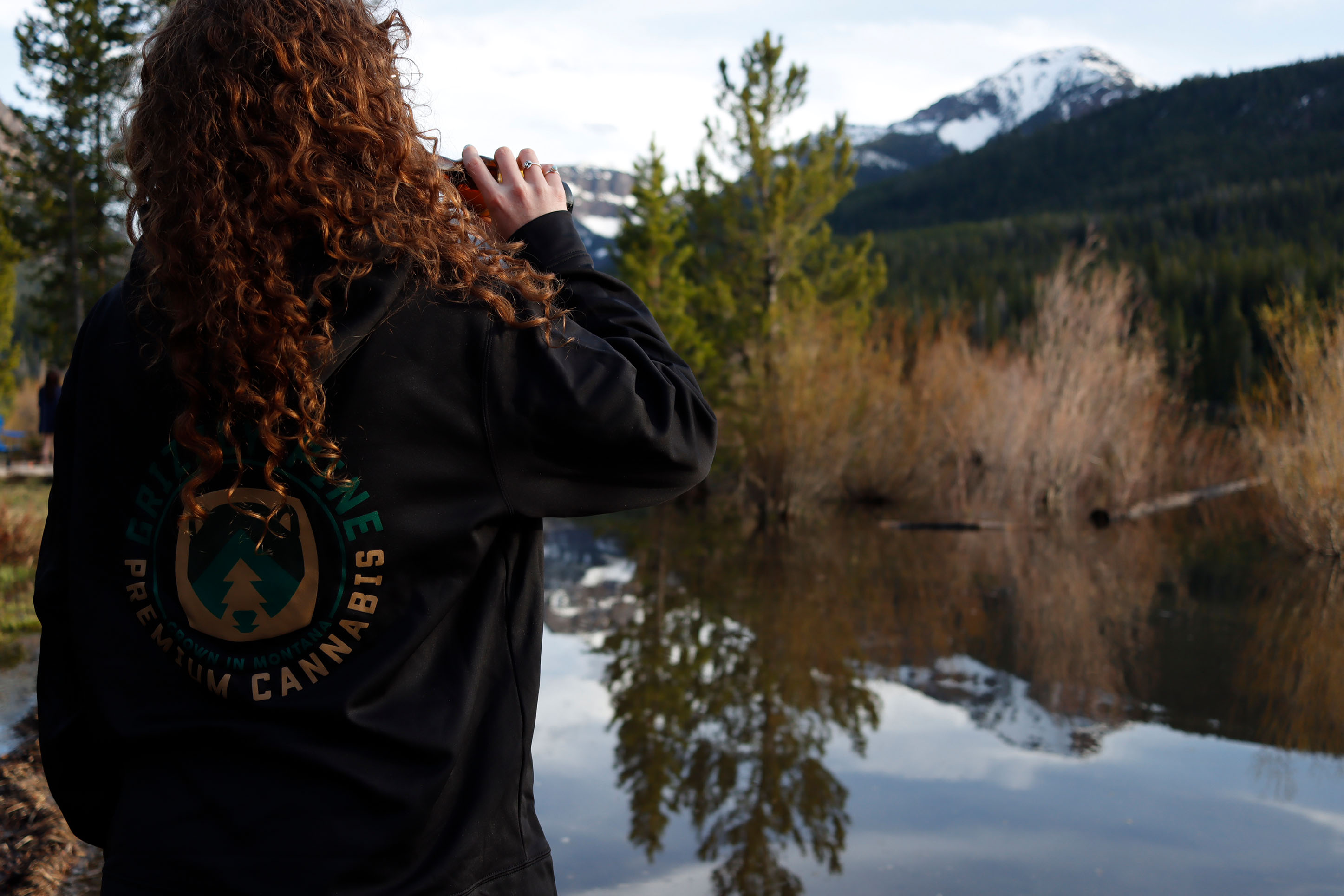 Photo of a woman drinking marijuana in a Grizzly Pine jacket in front of mountains