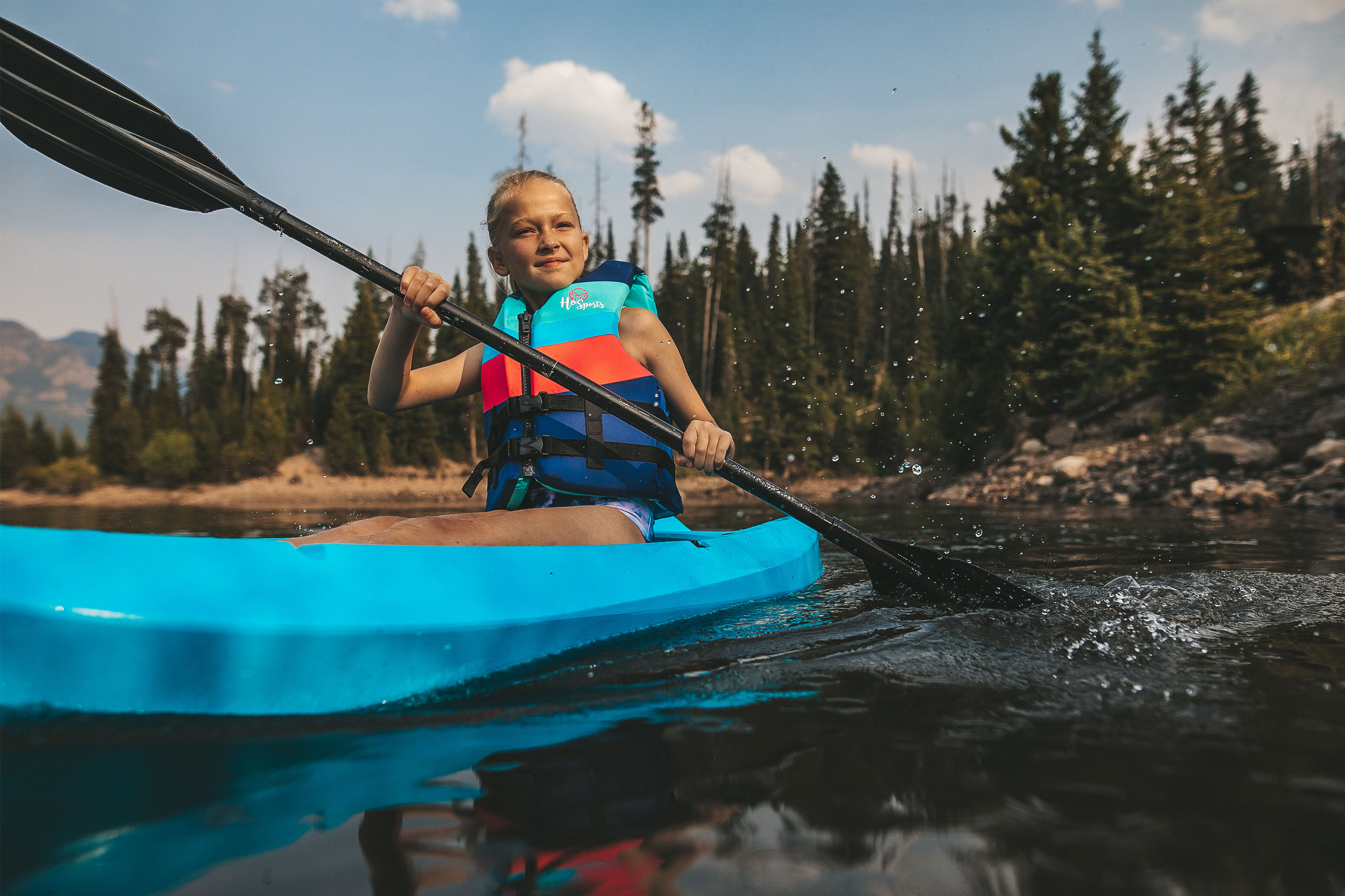 photo of a young girl sitting down on a paddle board, paddling in a reservoir