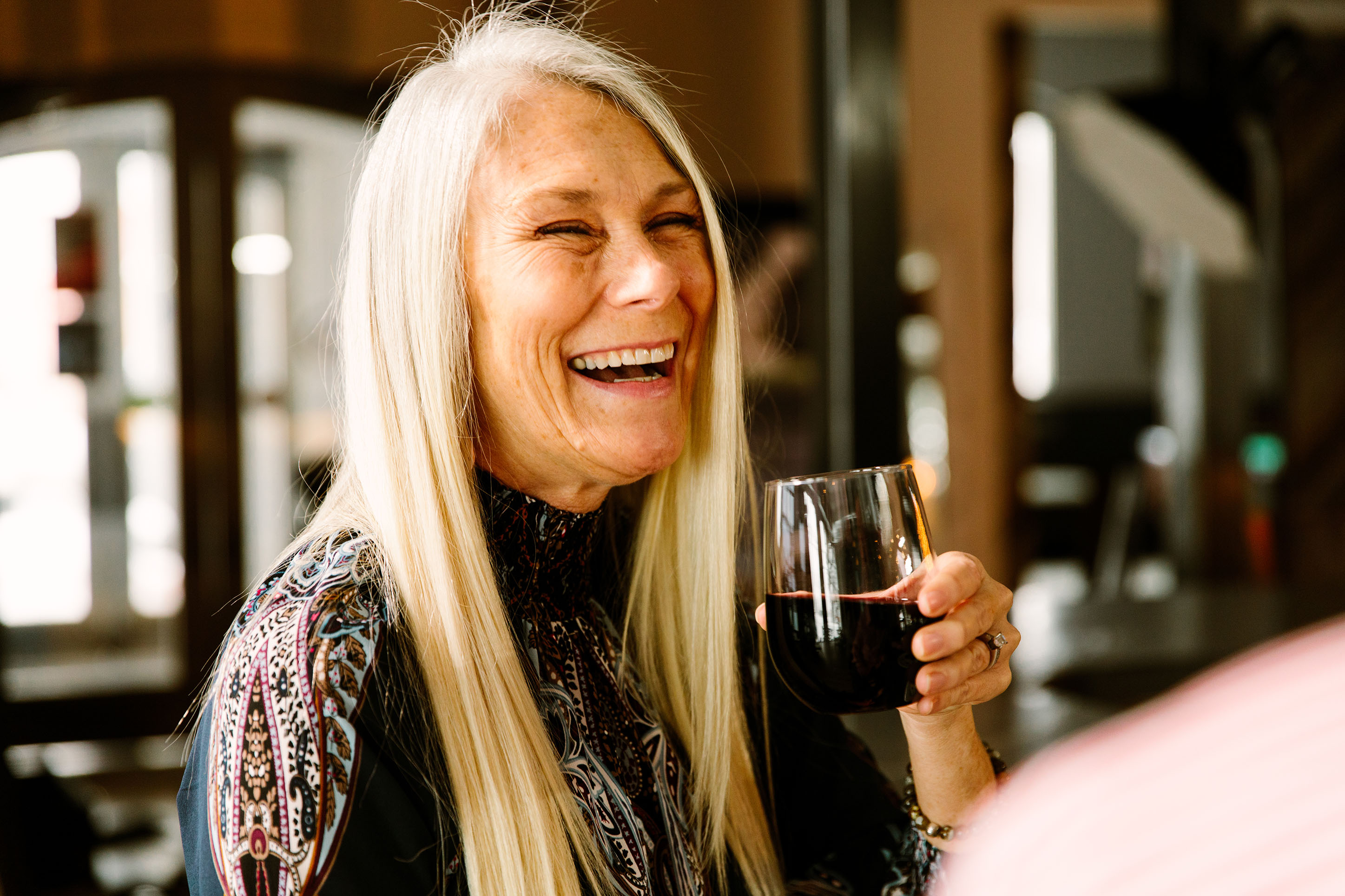 Photo of an older woman laughing with a glass of wine. 