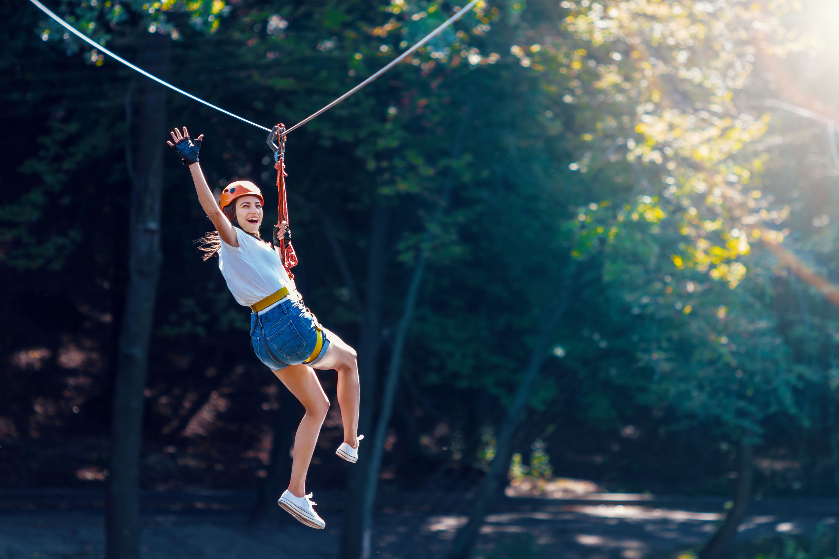 photo of a woman waving and smiling from a zipline in the forest