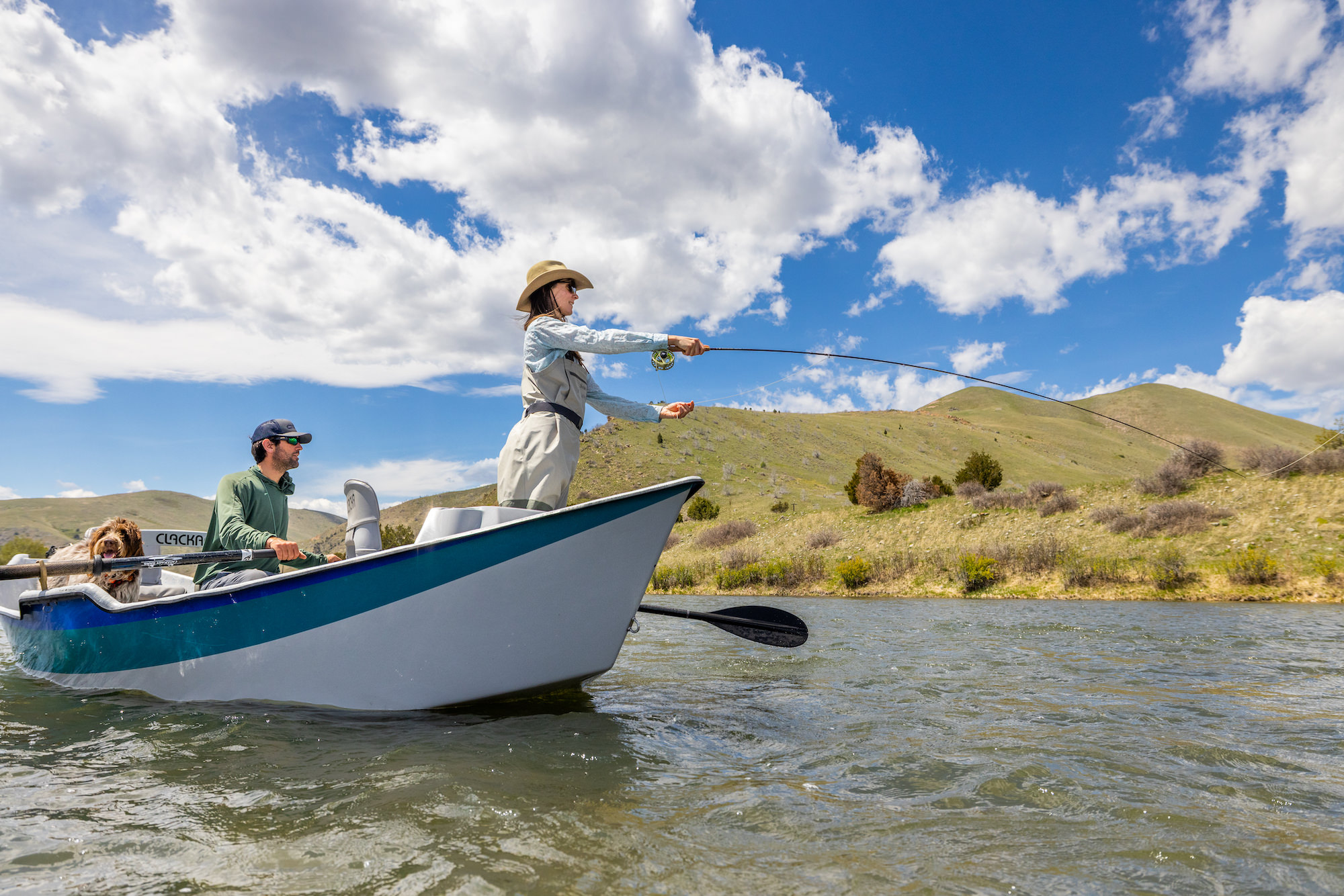 A man, woman, and dog float in a drift boat on the Madison River