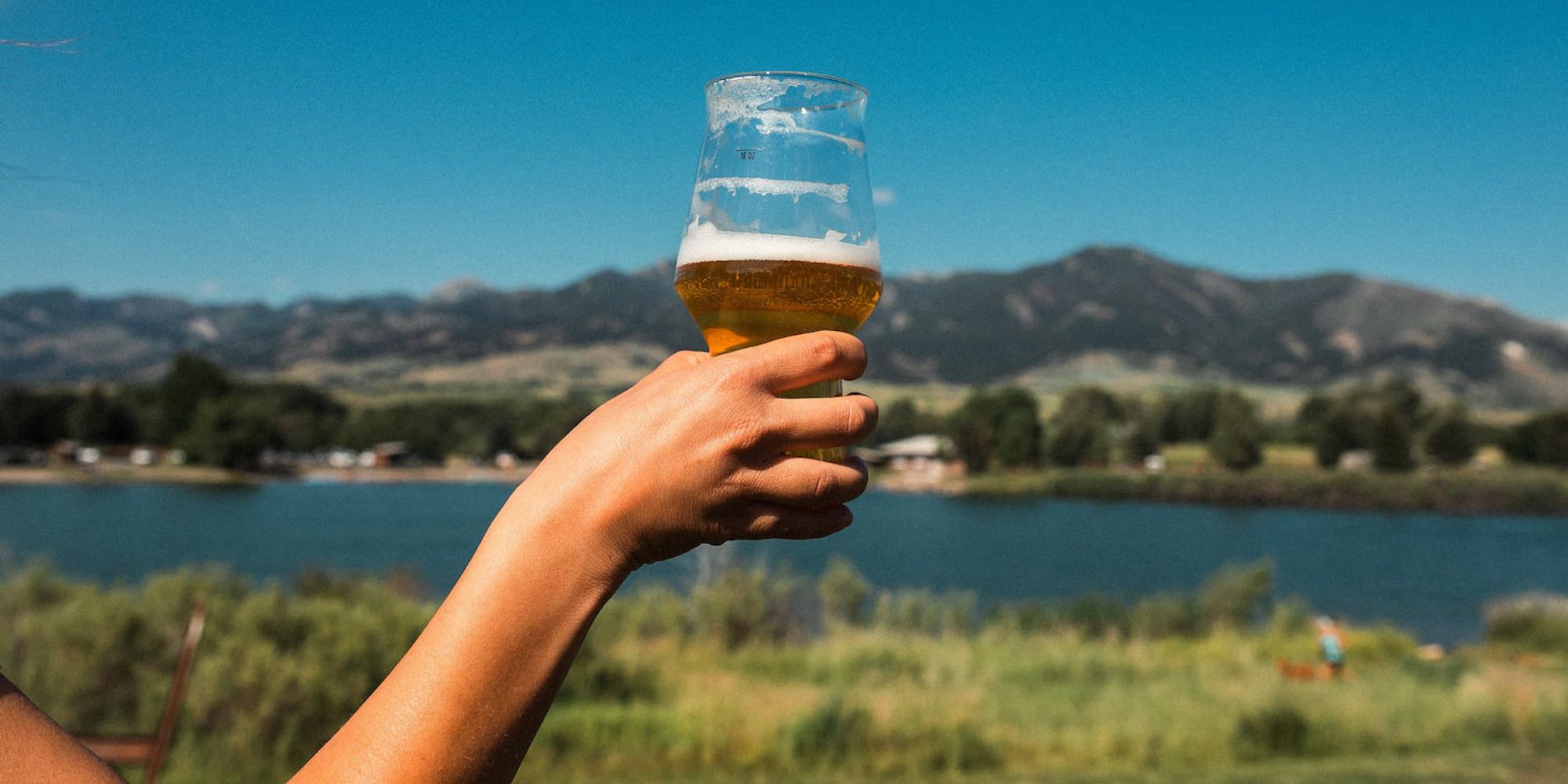 Hand holding a beer in front of a lake and the Bridger Mountains.